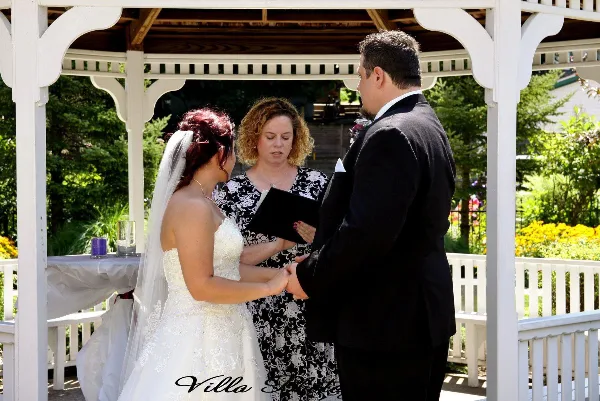 A wedding officiant performing a ceremony for a bride and groom under a white gazebo.