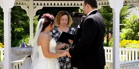 A wedding officiant performing a ceremony for a bride and groom under a white gazebo.