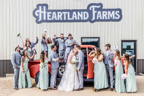 A wedding party poses with a vintage red truck in front of the Heartland Farms building.