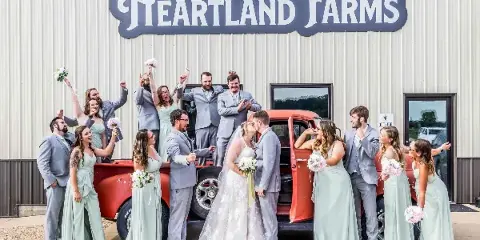 A wedding party poses with a vintage red truck in front of the Heartland Farms building.