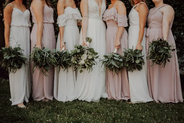 Bride and bridesmaids in white and pink dresses holding greenery bouquets
