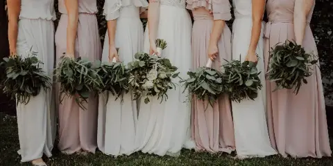 Bride and bridesmaids in white and pink dresses holding greenery bouquets