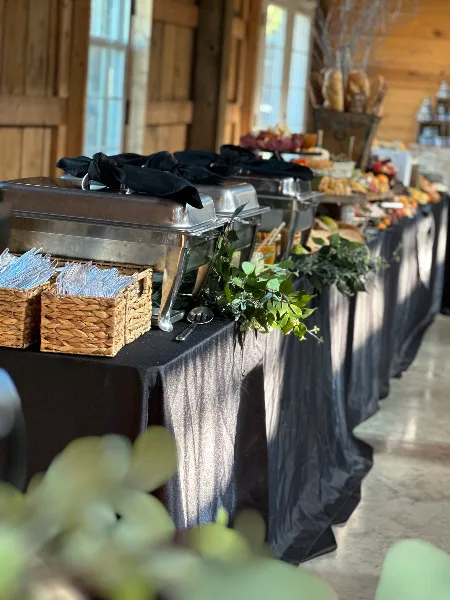 A catering buffet line featuring stainless steel chafing dishes, serving baskets, and a black tablecloth at an event venue.