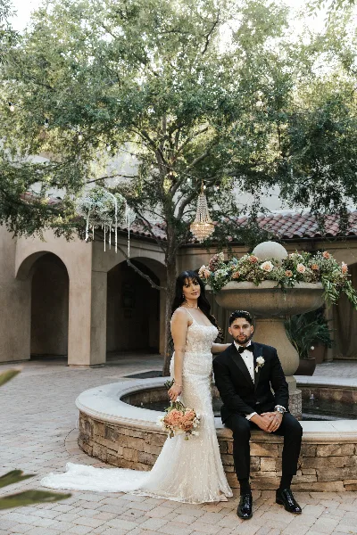 A bride and groom posing in a courtyard with a crystal chandelier and floral arrangements.