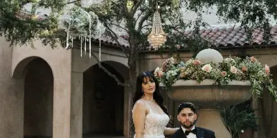 A bride and groom posing in a courtyard with a crystal chandelier and floral arrangements.