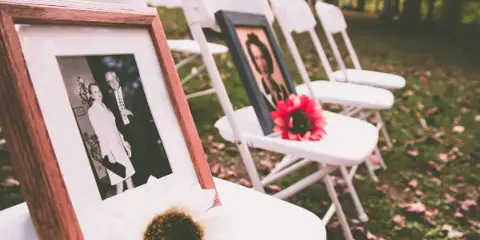 White folding chairs arranged in a row outdoors with framed photos and flowers placed on the seats.