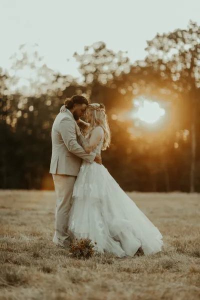A bride and groom embracing in a field during a sunset wedding photoshoot.
