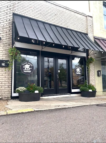 Exterior view of Sugar Daddy's Bakery storefront with black awning, glass doors, and business logo on windows.