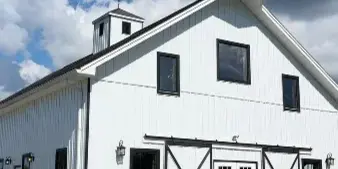 Exterior view of a white barn wedding venue with black trim and a cupola under a cloudy sky.