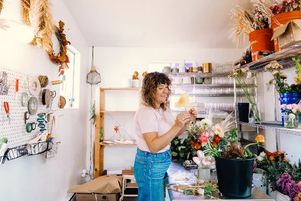 A florist arranging a bouquet in a bright studio workspace filled with fresh flowers and supplies.