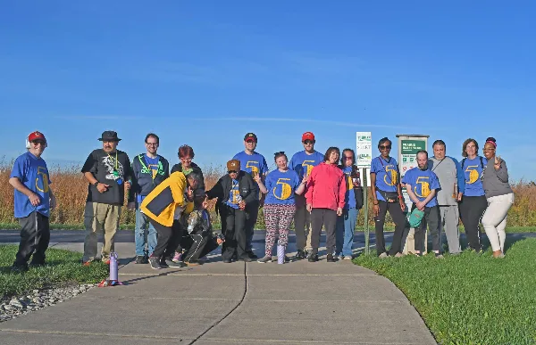 A group of people posing for a photo on a paved trail next to a sign for the Prairie Bluff Trail.