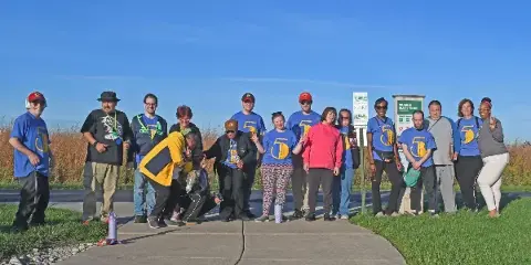 A group of people posing for a photo on a paved trail next to a sign for the Prairie Bluff Trail.
