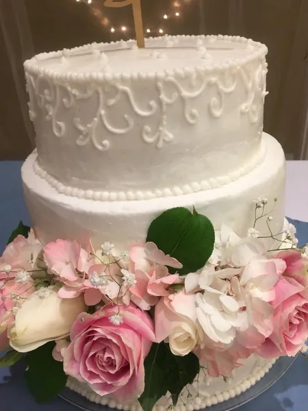 A two-tier white wedding cake with piped floral designs and a fresh flower arrangement at the base.