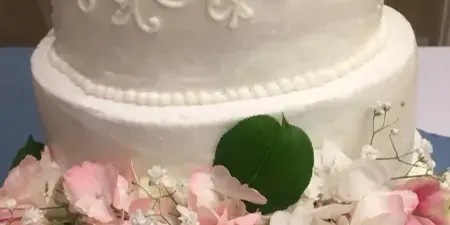 A two-tier white wedding cake with piped floral designs and a fresh flower arrangement at the base.