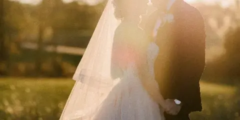 A bride and groom holding hands in a field during golden hour, with the bride's veil illuminated by the sun.
