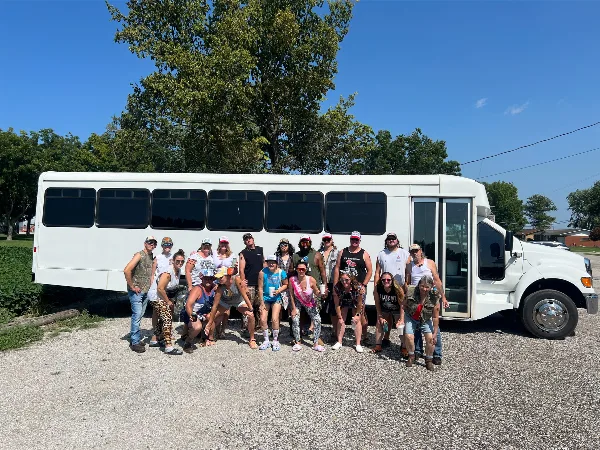 A group of people posing in front of a white shuttle bus on a gravel lot.