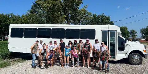 A group of people posing in front of a white shuttle bus on a gravel lot.