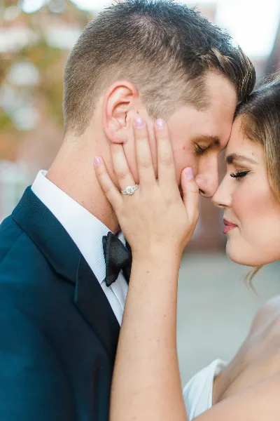 A close-up fine art wedding photograph of a bride and groom sharing an intimate moment, with the bride's hand gently touching the groom's face.