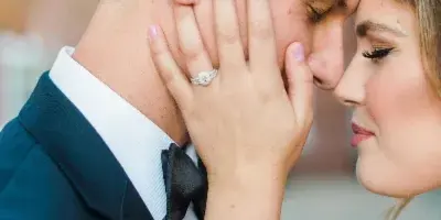 A close-up fine art wedding photograph of a bride and groom sharing an intimate moment, with the bride's hand gently touching the groom's face.