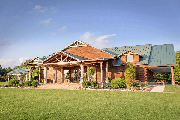 Exterior view of a rustic wooden lodge venue with a green metal roof and large front lawn.