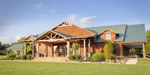 Exterior view of a rustic wooden lodge venue with a green metal roof and large front lawn.
