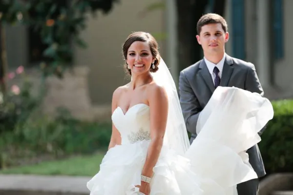 A bride in a white wedding dress and veil standing next to a groom in a grey suit.