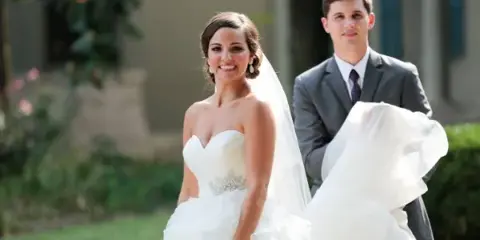 A bride in a white wedding dress and veil standing next to a groom in a grey suit.