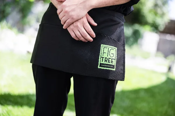 A catering staff member wearing a black apron with the Fig Tree Catering Co. logo.