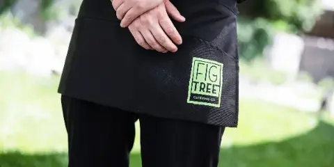 A catering staff member wearing a black apron with the Fig Tree Catering Co. logo.