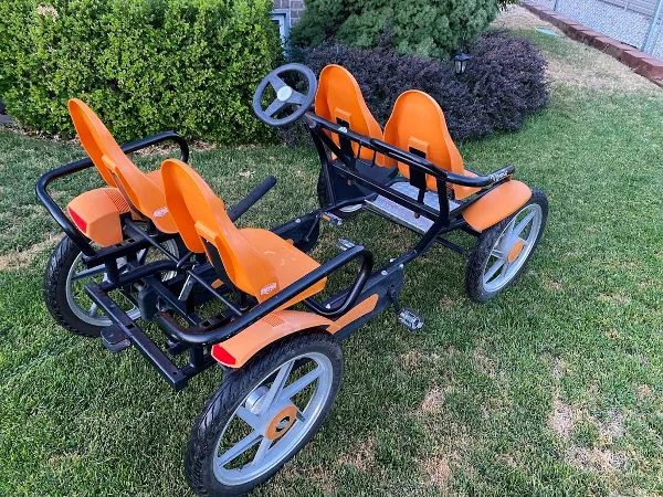 Two orange and black multi-passenger pedal cycles parked on a grassy lawn.
