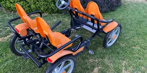 Two orange and black multi-passenger pedal cycles parked on a grassy lawn.