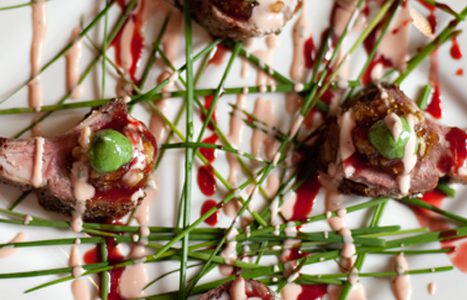 A close-up of a plated gourmet dish featuring meat, green garnish, and artistic sauce drizzles.