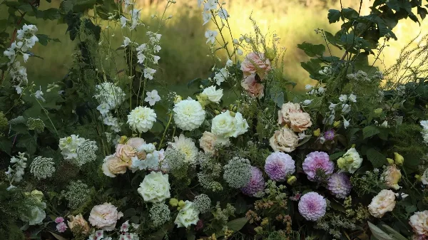 A close-up of a lush floral arrangement featuring white and pink roses, dahlias, and greenery.