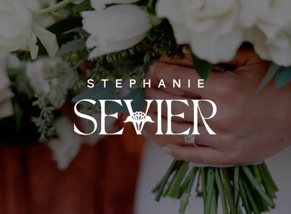 Close-up of a hand holding a white wedding bouquet with an engagement ring visible, overlaid with the text 'STEPHANIE SEVIER'.