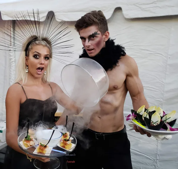 Two servers presenting plated appetizers with a dry-ice smoke effect at an event.