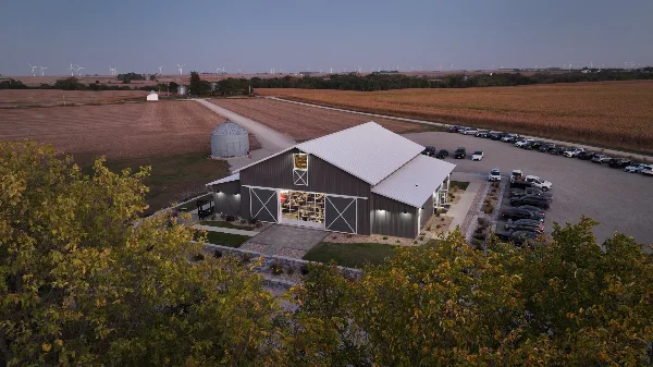 Aerial view of a modern barn-style wedding venue surrounded by rural farmland and a parking lot at dusk.