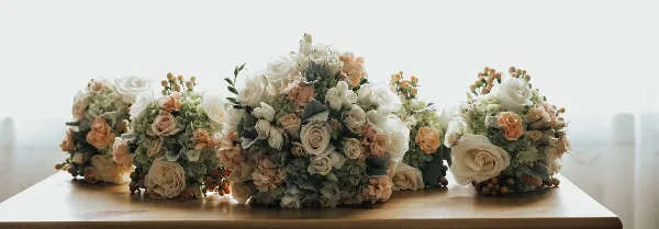 A collection of white and peach floral centerpieces arranged on a wooden table.