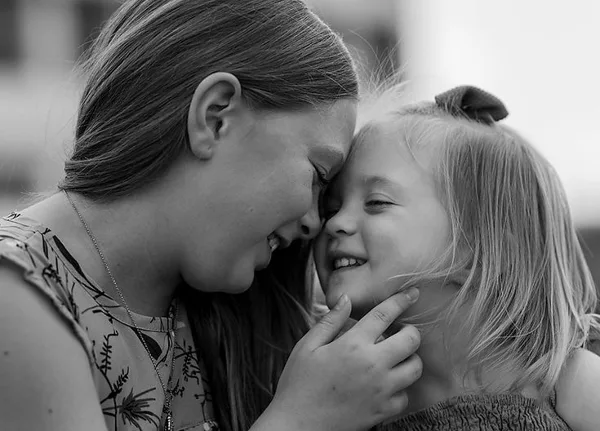 A black-and-white portrait of a smiling woman gently touching the chin of a young girl.