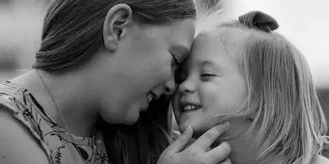 A black-and-white portrait of a smiling woman gently touching the chin of a young girl.