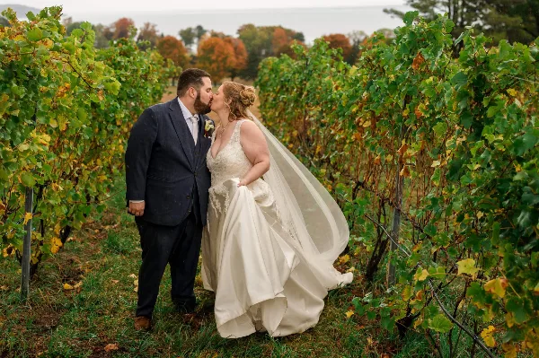 A bride and groom sharing a kiss in a vineyard during a wedding photoshoot.