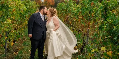A bride and groom sharing a kiss in a vineyard during a wedding photoshoot.