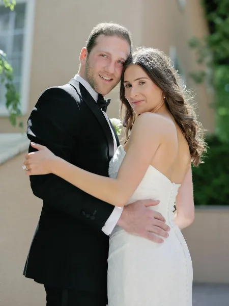 A bride with styled hair and makeup embracing a groom in a tuxedo.