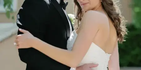 A bride with styled hair and makeup embracing a groom in a tuxedo.