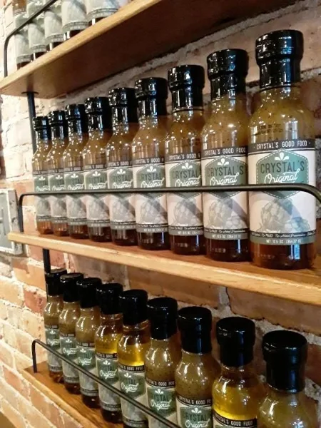 Rows of bottled Crystal's Original salad dressing with Crystal's Good Food labels displayed on wooden shelves against a brick wall.