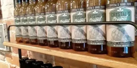 Rows of bottled Crystal's Original salad dressing with Crystal's Good Food labels displayed on wooden shelves against a brick wall.