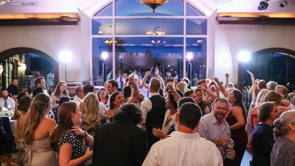 A crowded wedding dance floor with guests dancing under event lighting.