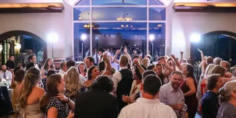 A crowded wedding dance floor with guests dancing under event lighting.