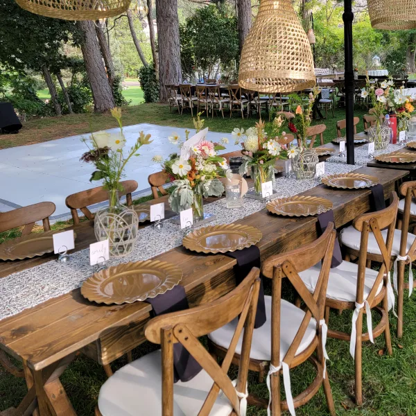 Outdoor event setup with wooden tables, chairs, and floral centerpieces