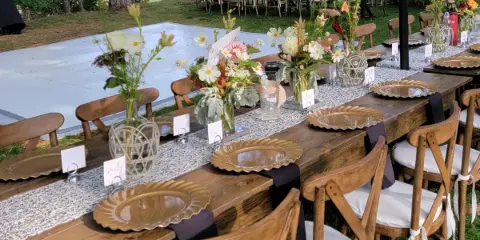 Outdoor event setup with wooden tables, chairs, and floral centerpieces
