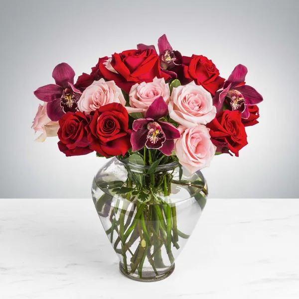 A floral arrangement featuring red and pink roses and purple orchids in a clear glass vase.